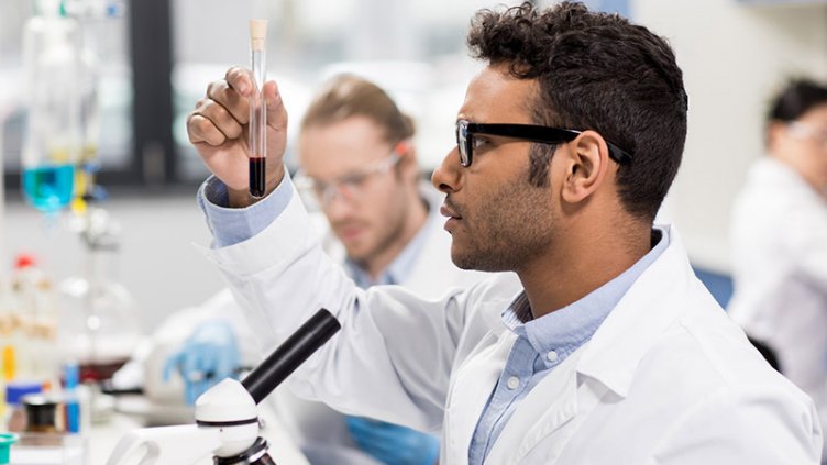 Side view of young scientist in eyeglasses looking at test tube in research laboratory
