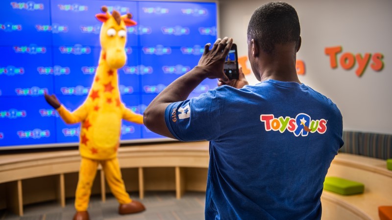 A man clicking a picture of giraffe costumed man 