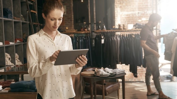 Retailer looking at the tablet while customer choosing t-shirt